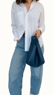 A person wearing a white shirt and blue jeans, holding a navy-colored mini tote bag with a leather shoulder strap.
