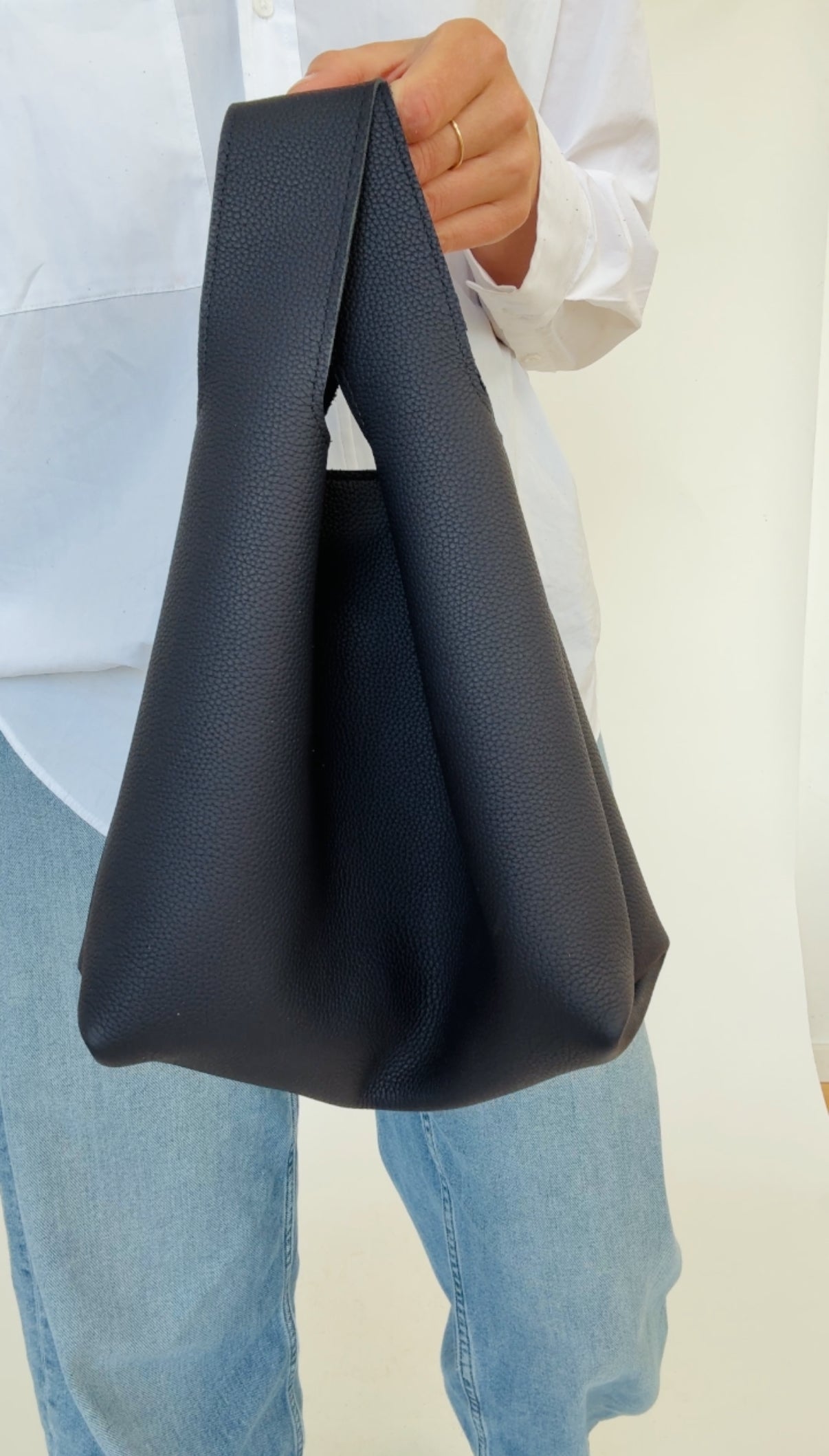 A person holding a dark navy mini tote bag with a shoulder strap.
