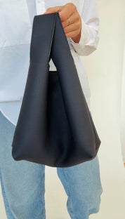 A person holding a dark navy mini tote bag with a shoulder strap.