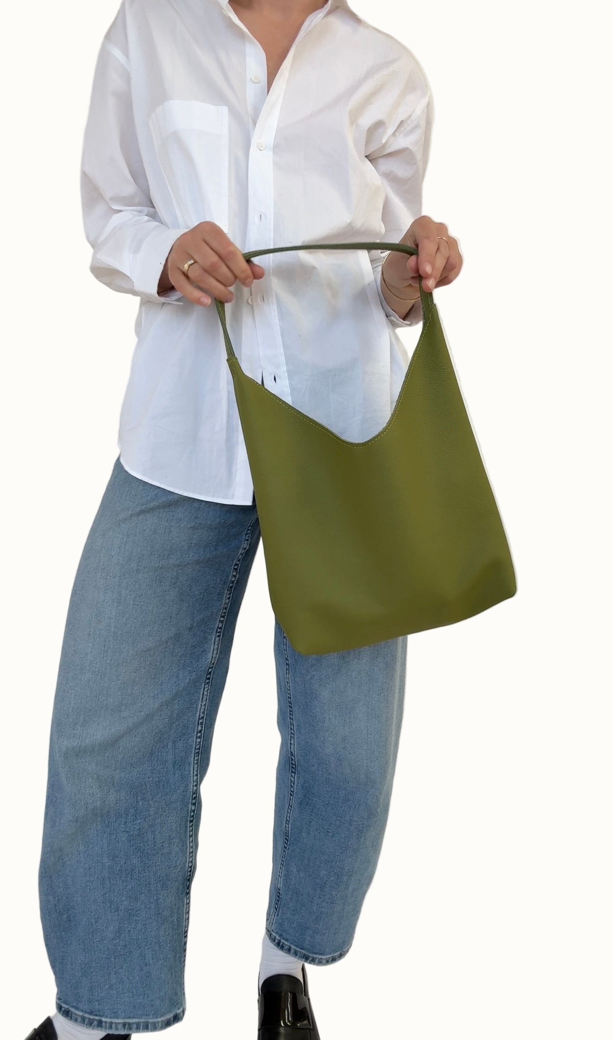 A person wearing a white shirt and blue jeans is holding a green shoulder bag over their shoulder.