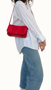Person wearing a white shirt, blue jeans, and black shoes with a red handbag on a plain background