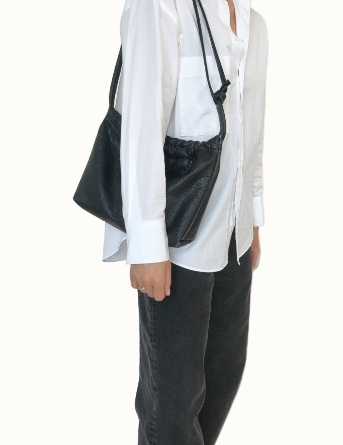 Person wearing a white shirt and black pants with a black bag over one shoulder against a plain background