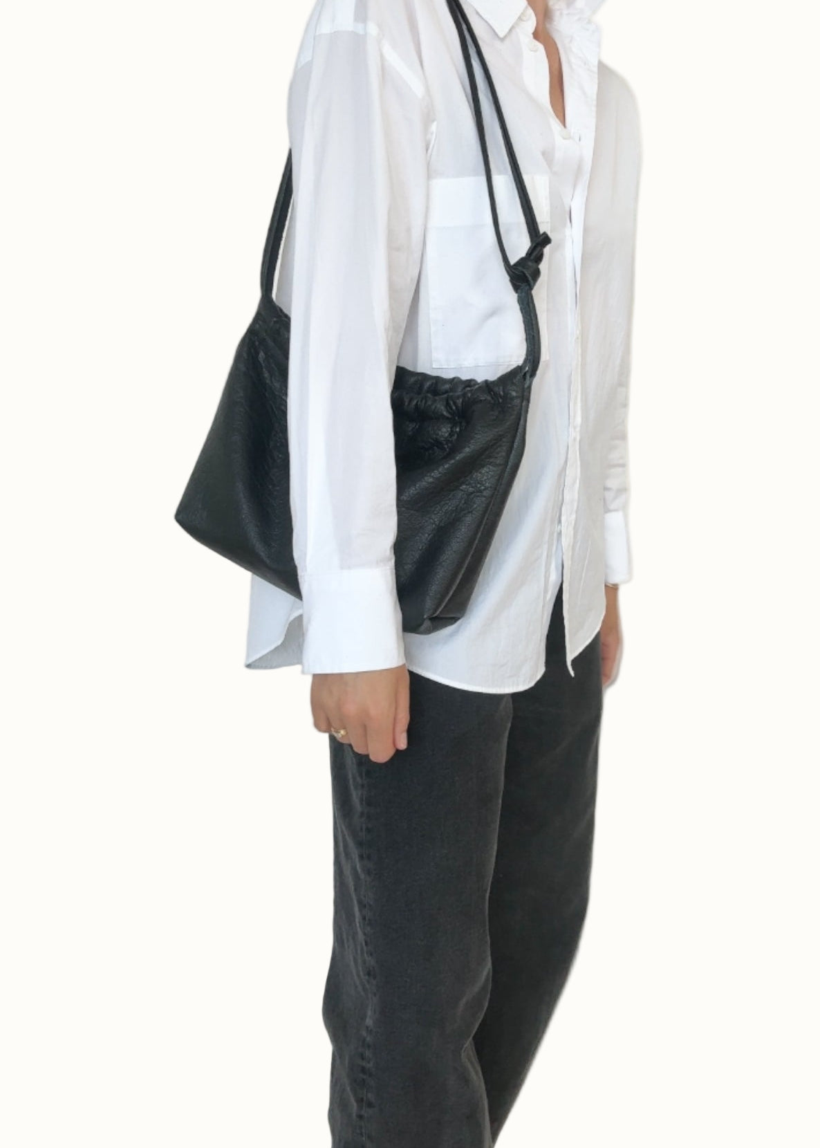 Person wearing a white shirt and black pants with a black bag over one shoulder against a plain background