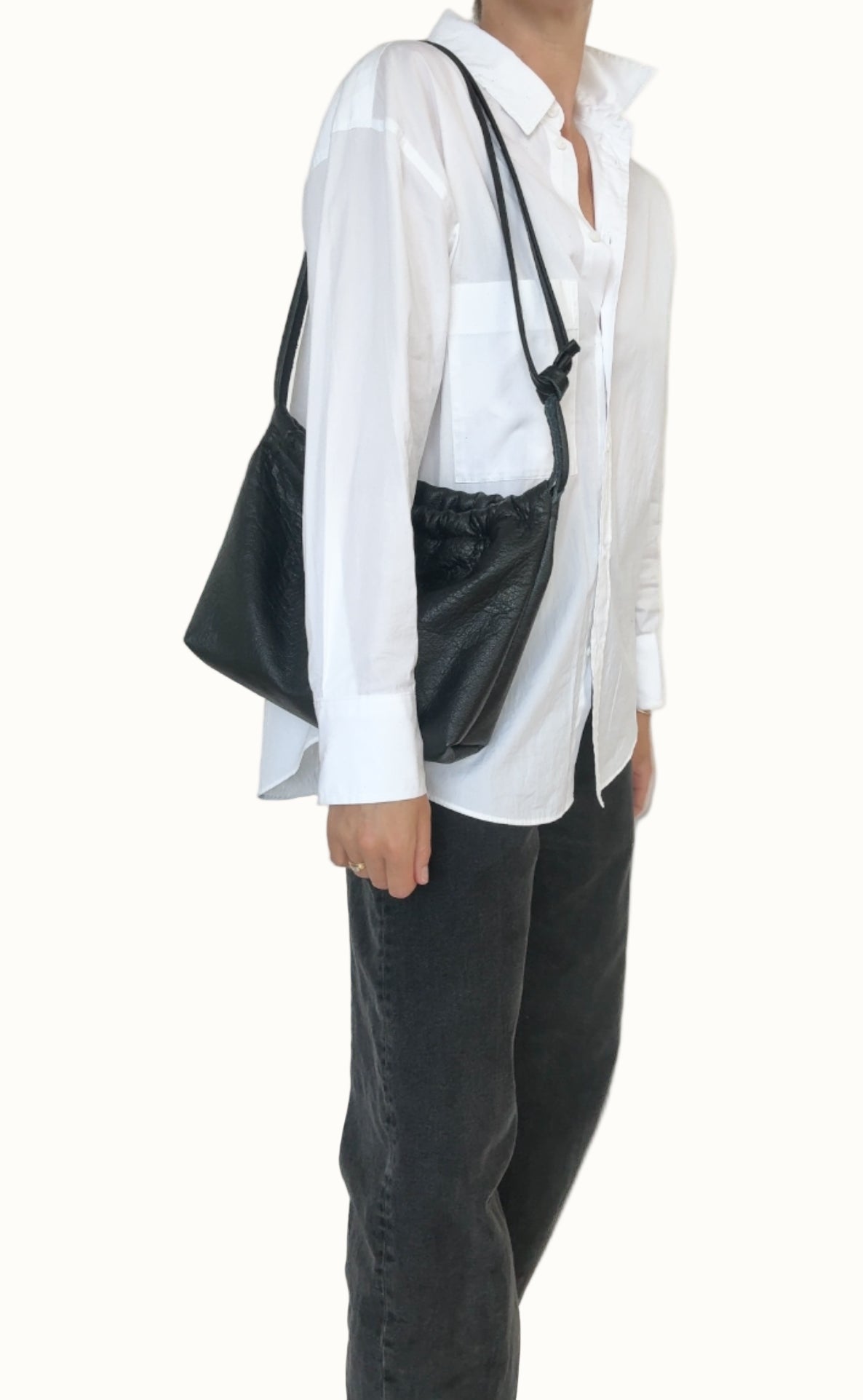 Person wearing a white shirt and black pants with a black bag over one shoulder against a plain background