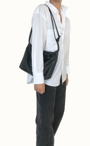 Person wearing a white shirt and black pants with a black bag over one shoulder against a plain background