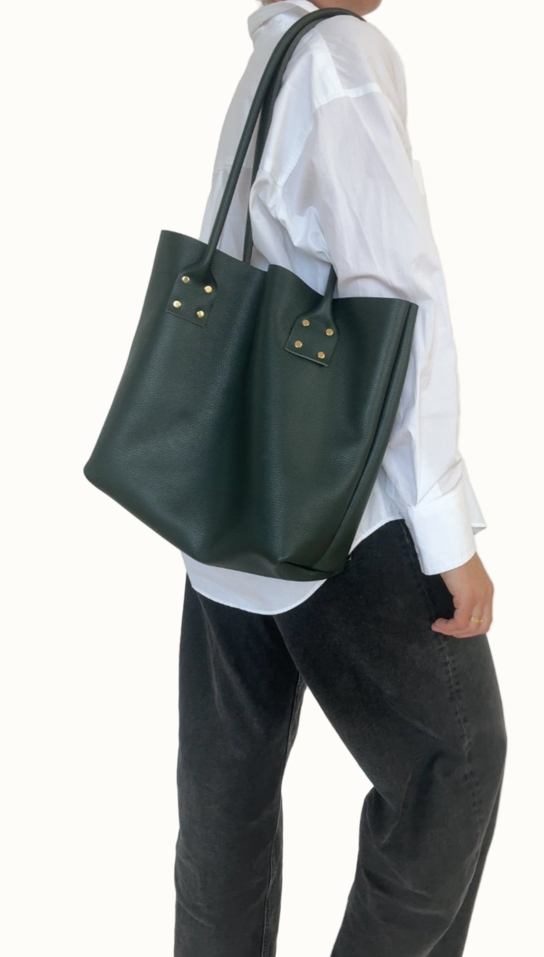 Person wearing a white shirt and dark green tote bag on a plain background