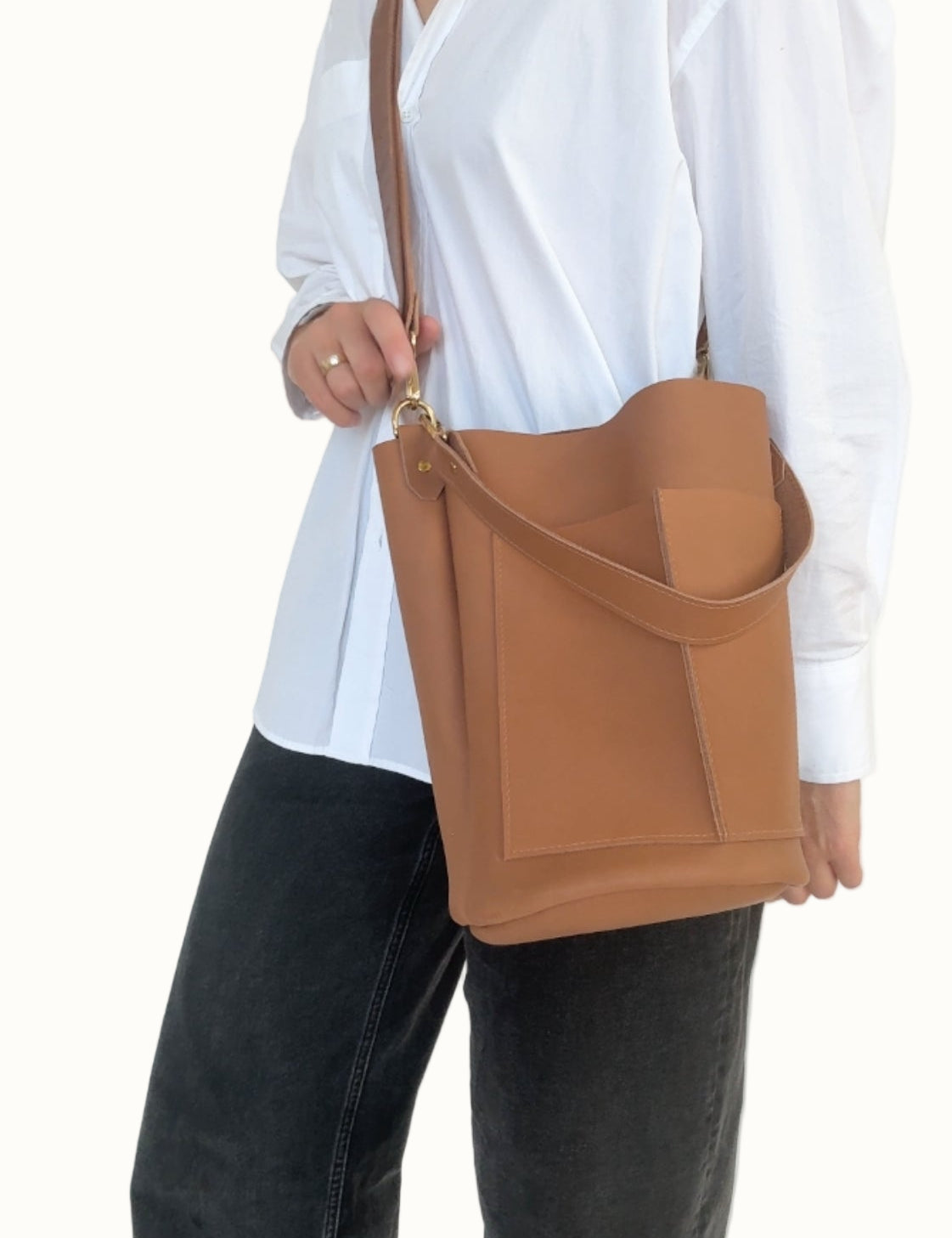 Person wearing a white shirt and black pants holding a brown leather bag against a white background