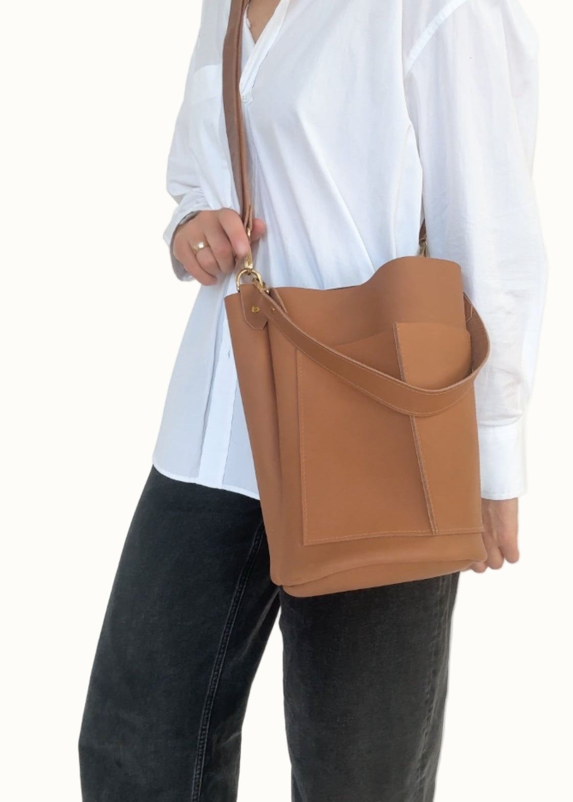 Person wearing a white shirt and black pants holding a brown leather bag against a white background