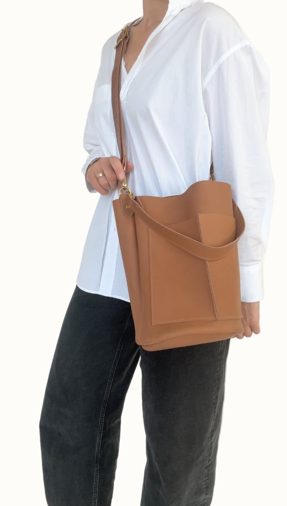 Person wearing a white shirt and black pants holding a brown leather bag against a white background