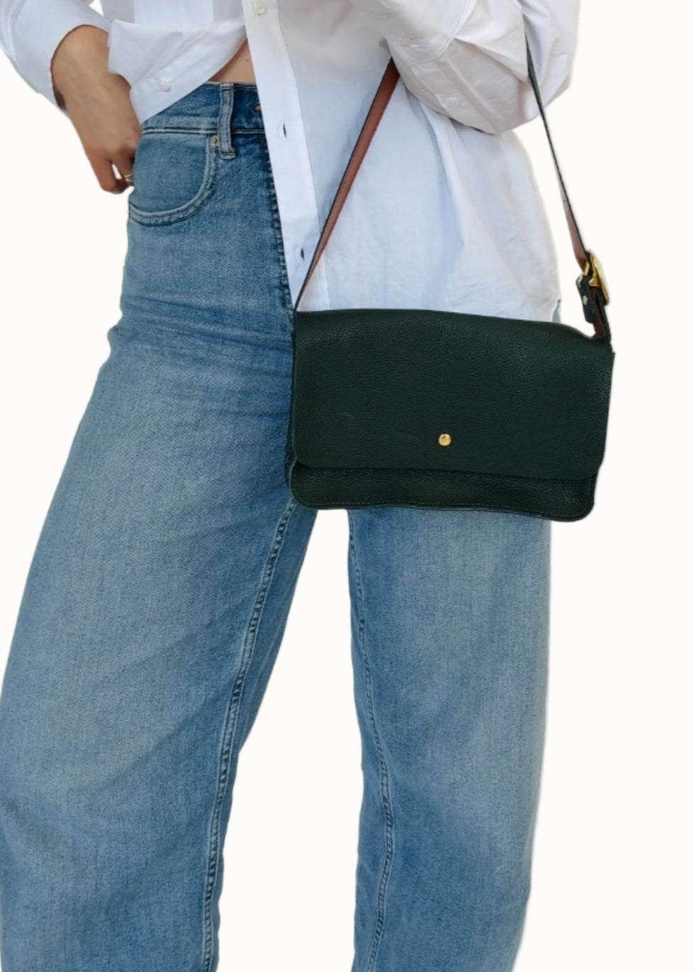 A person wearing a white shirt and blue jeans is holding a cream-colored crossbody bag with a leather strap and a compact design.