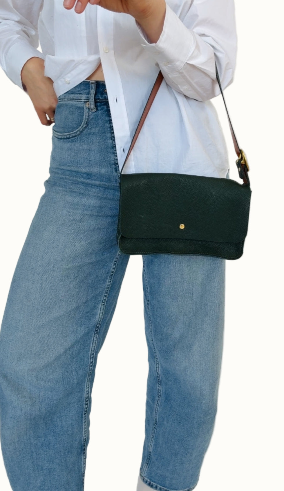 A person wearing a white shirt and blue jeans is holding a cream-colored crossbody bag with a leather strap and a compact design.
