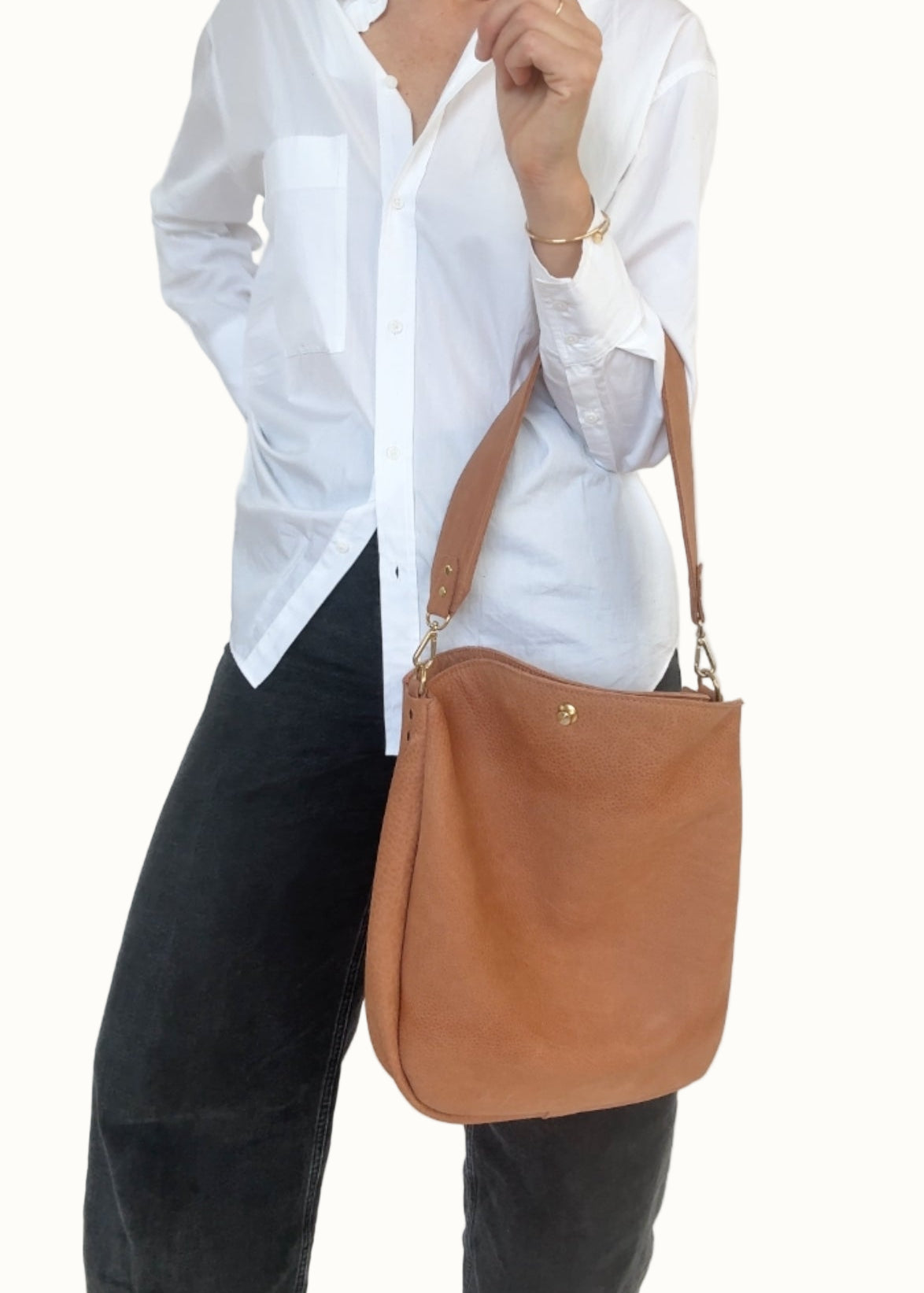 Person wearing a white shirt and black pants with a brown shoulder bag against a white background