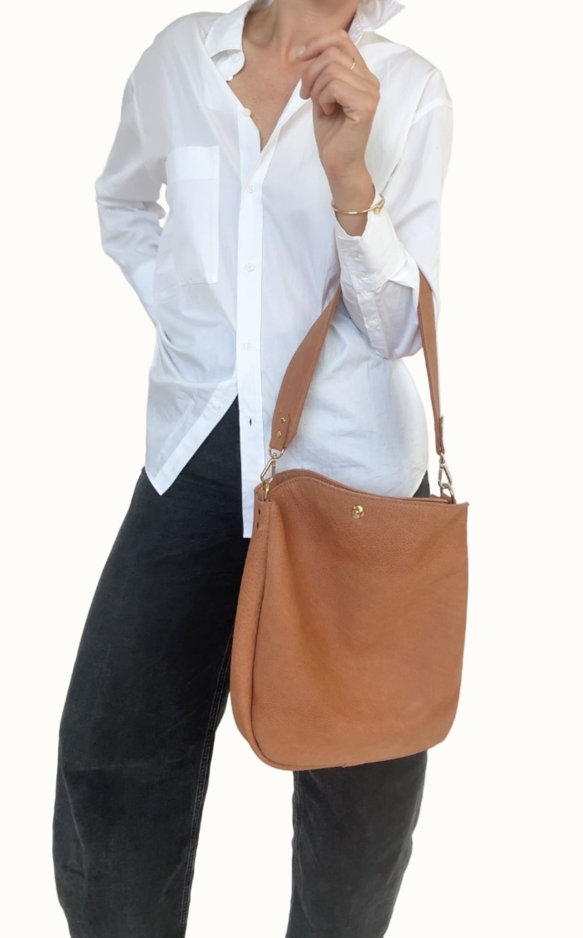 Person wearing a white shirt and black pants with a brown shoulder bag against a white background