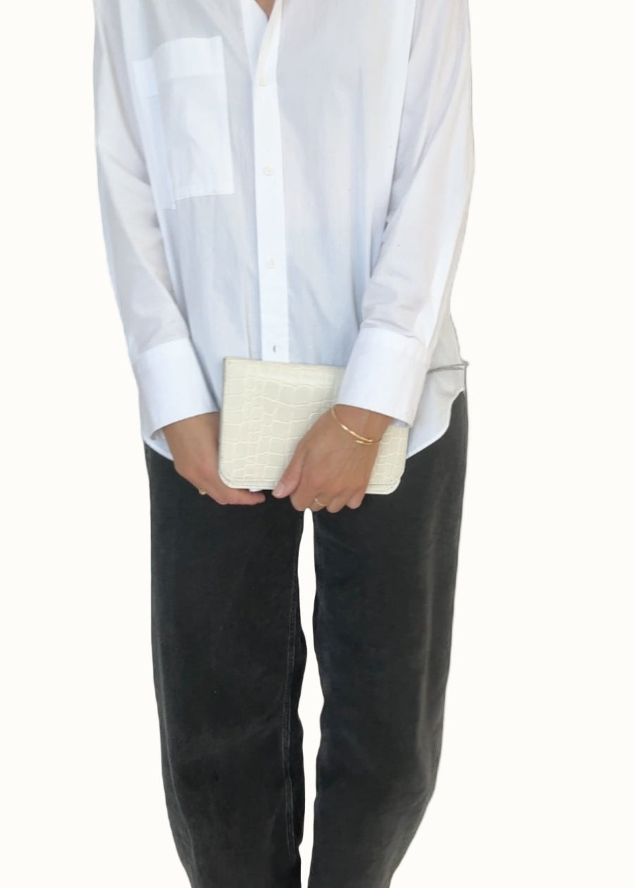 Person wearing a white shirt and black pants holding a beige clutch against a white background