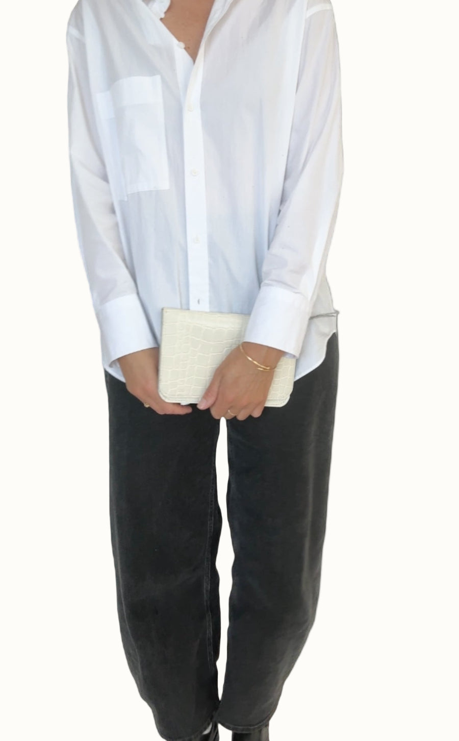 Person wearing a white shirt and black pants holding a beige clutch against a white background