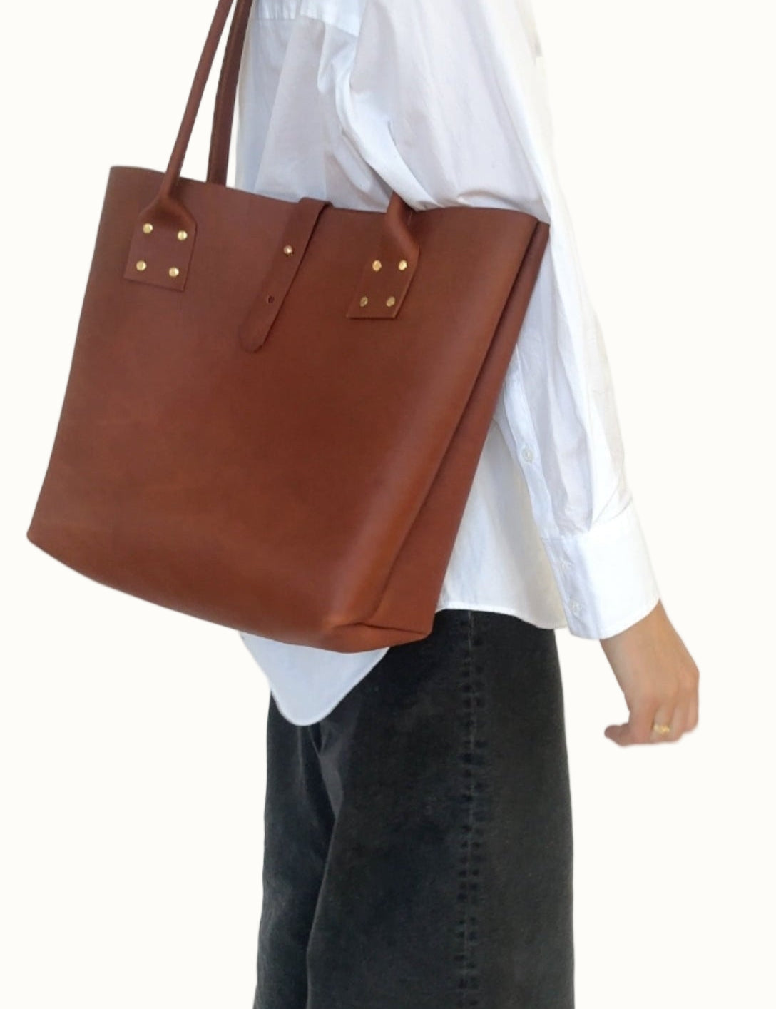 Person wearing a white shirt and dark jeans holding a brown leather tote bag.