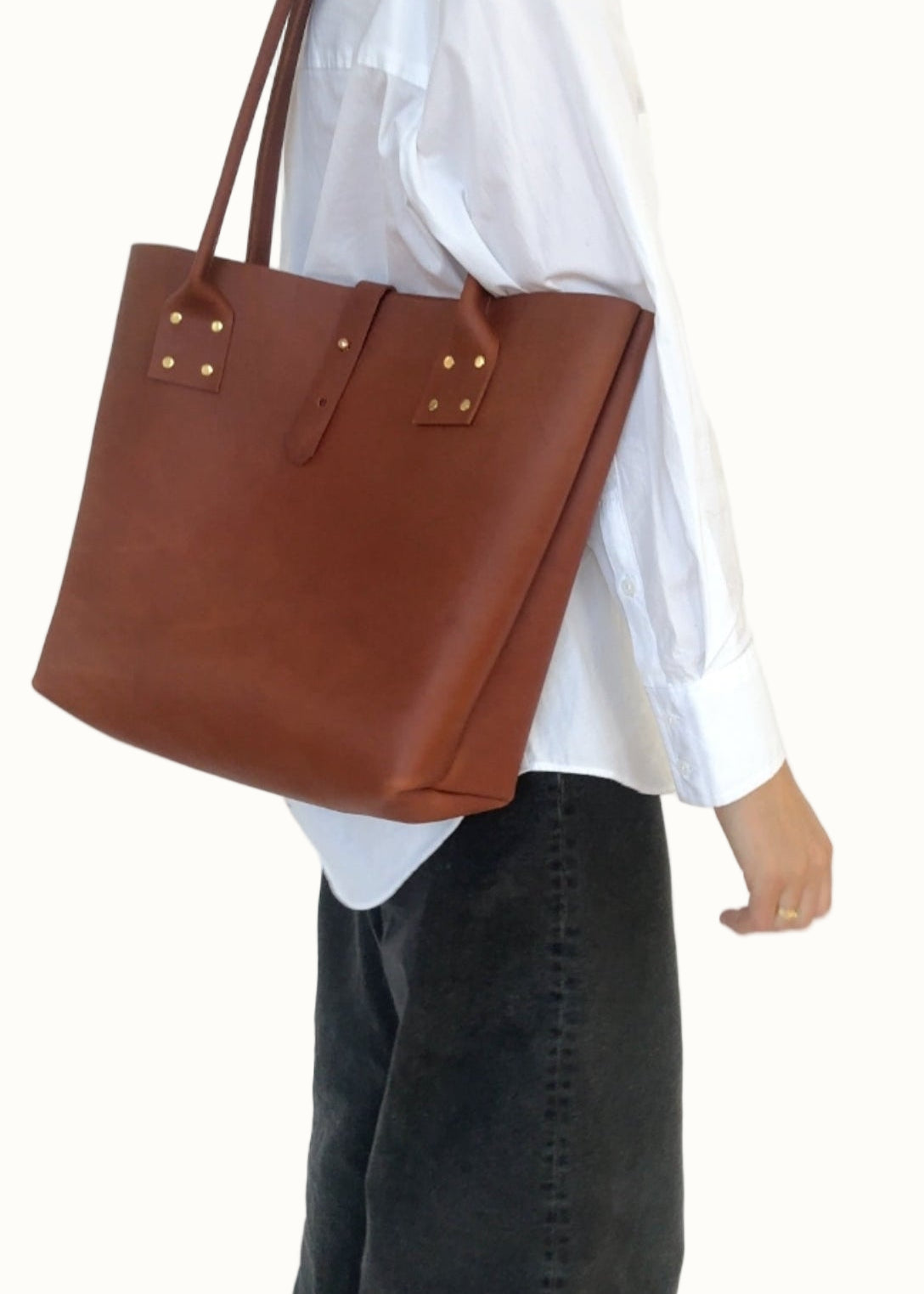 Person wearing a white shirt and dark jeans holding a brown leather tote bag.