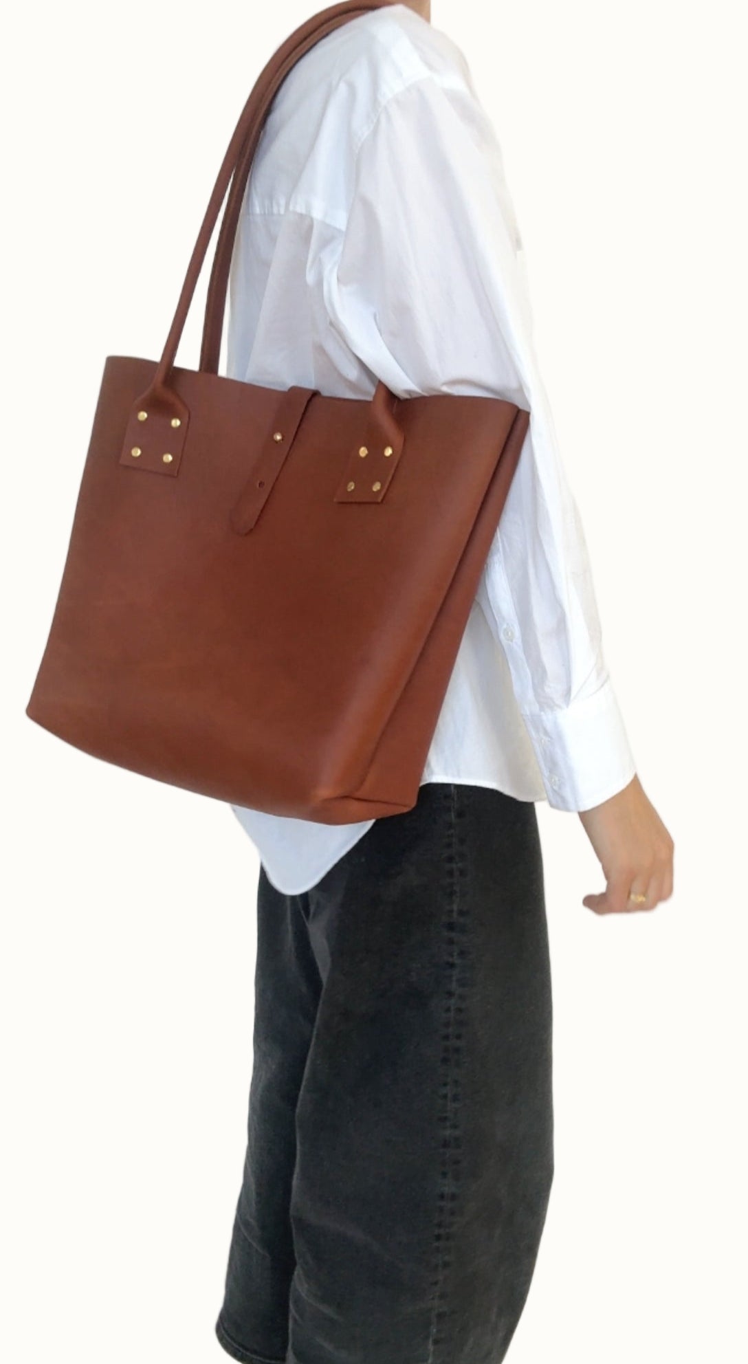 Person wearing a white shirt and dark jeans holding a brown leather tote bag.