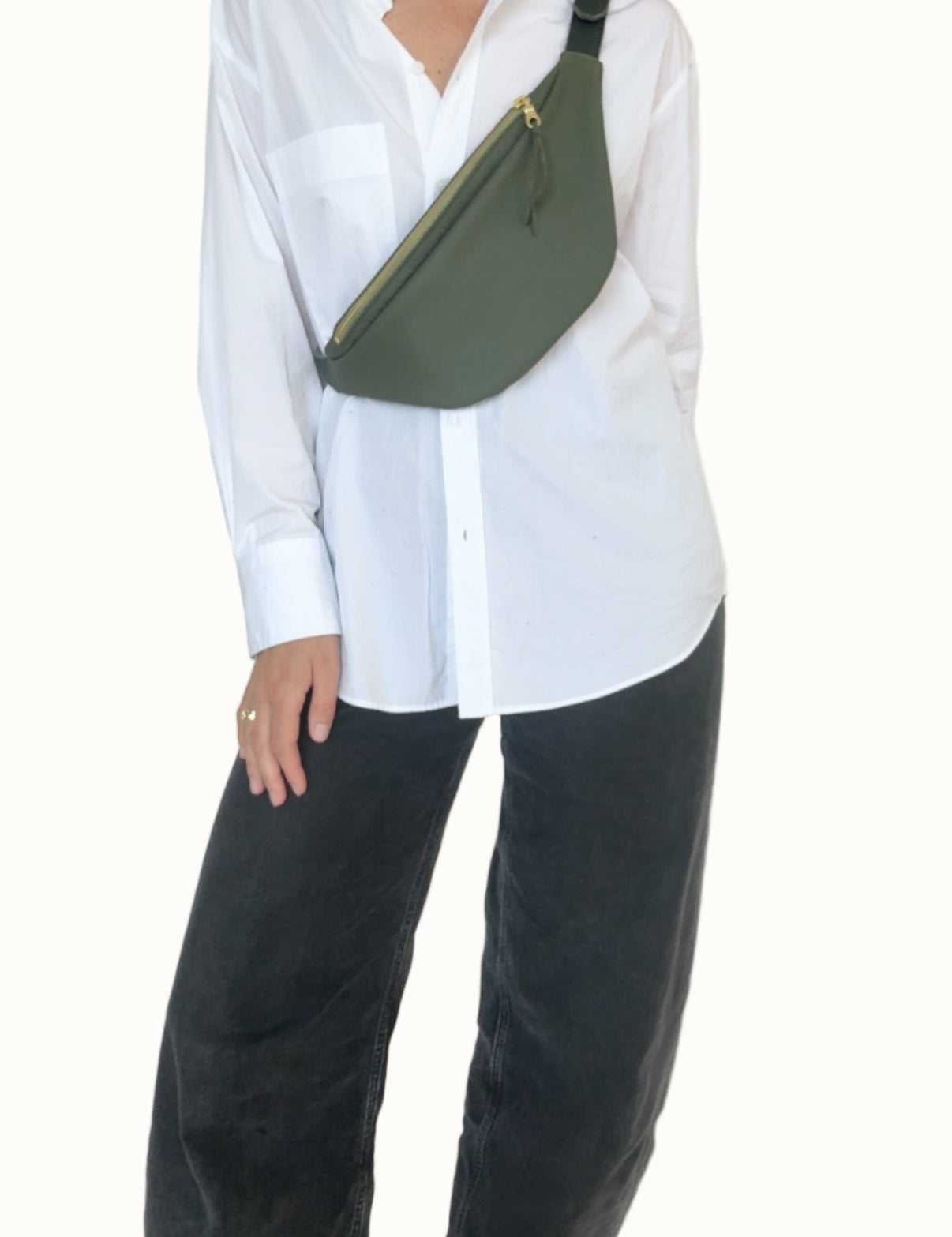 Person wearing a white shirt and black pants with a green sling bag on a plain background
