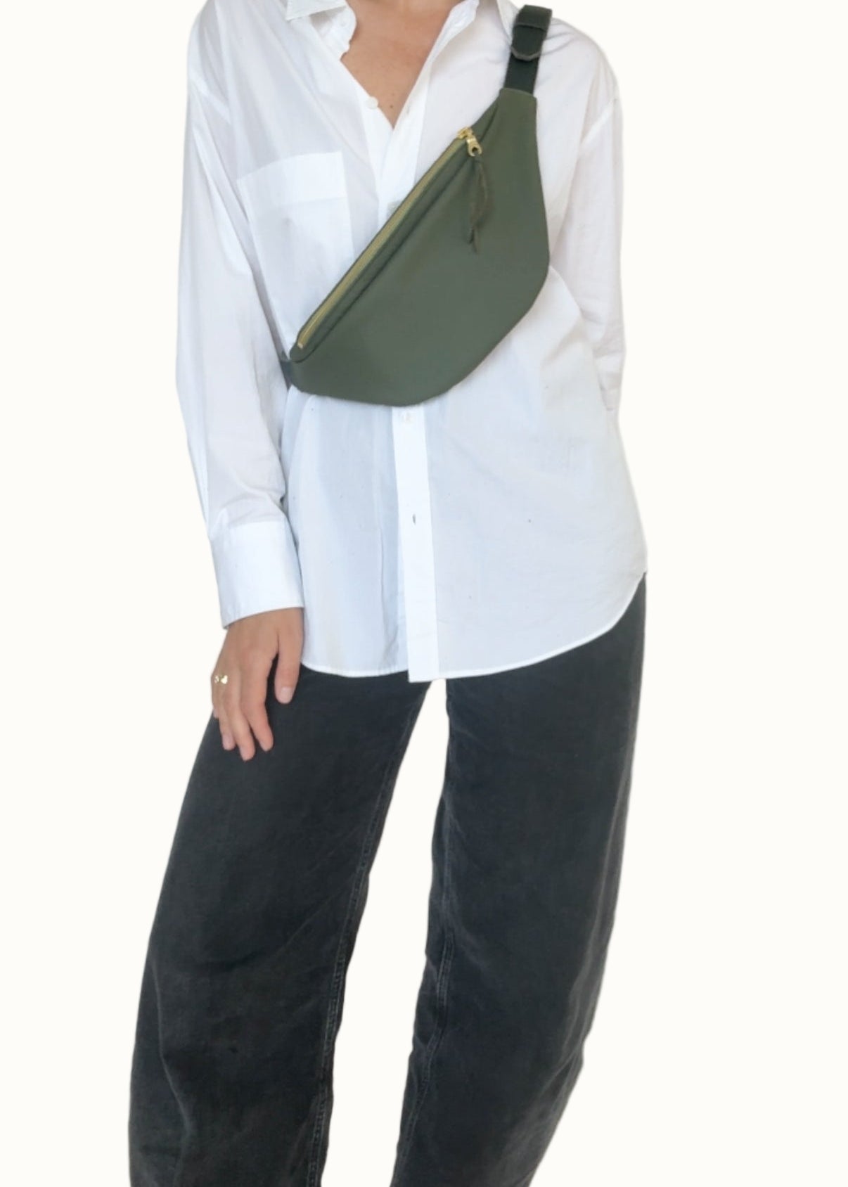 Person wearing a white shirt and black pants with a green sling bag on a plain background