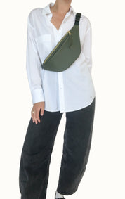 Person wearing a white shirt and black pants with a green sling bag on a plain background