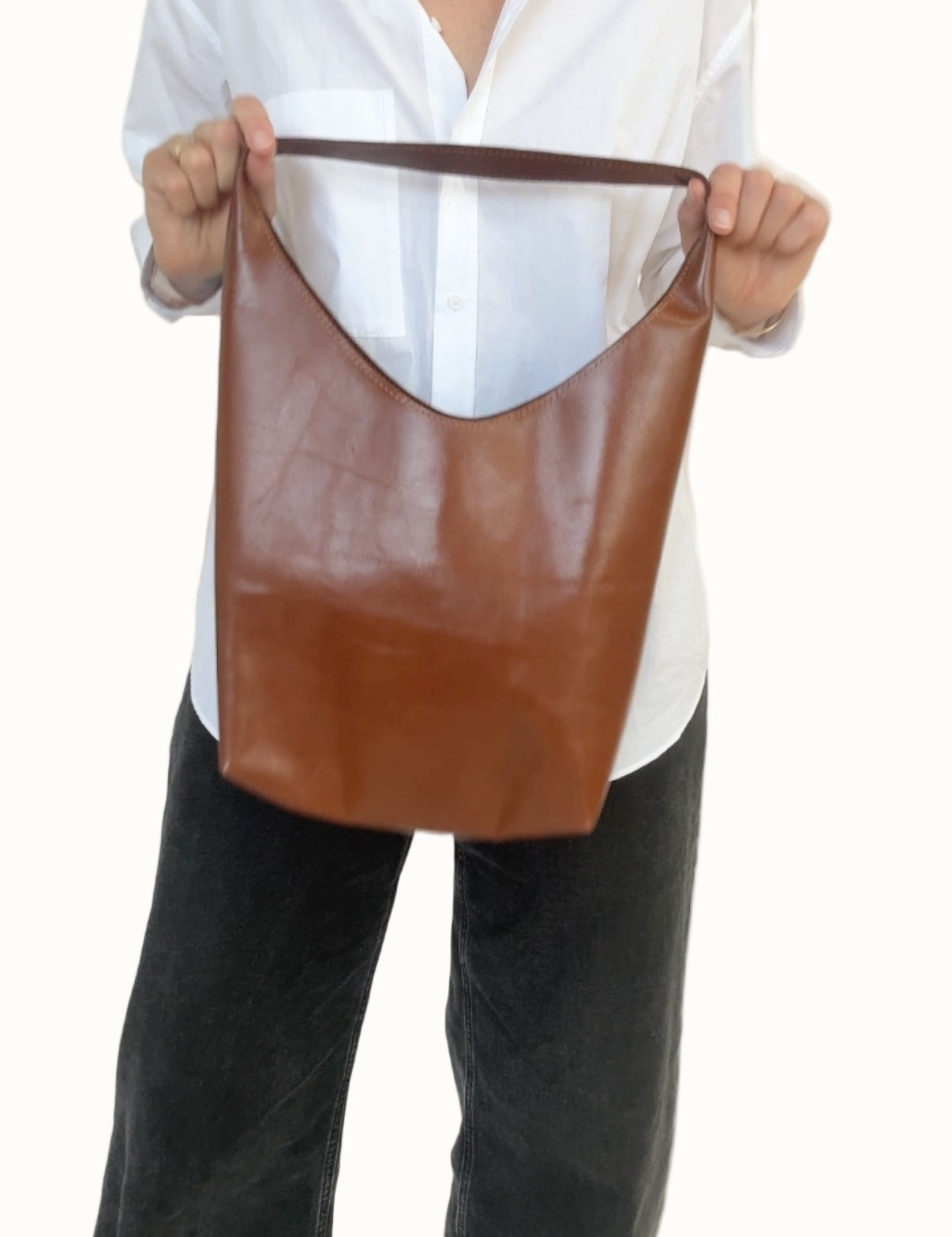 Person holding a brown leather tote bag against a white background