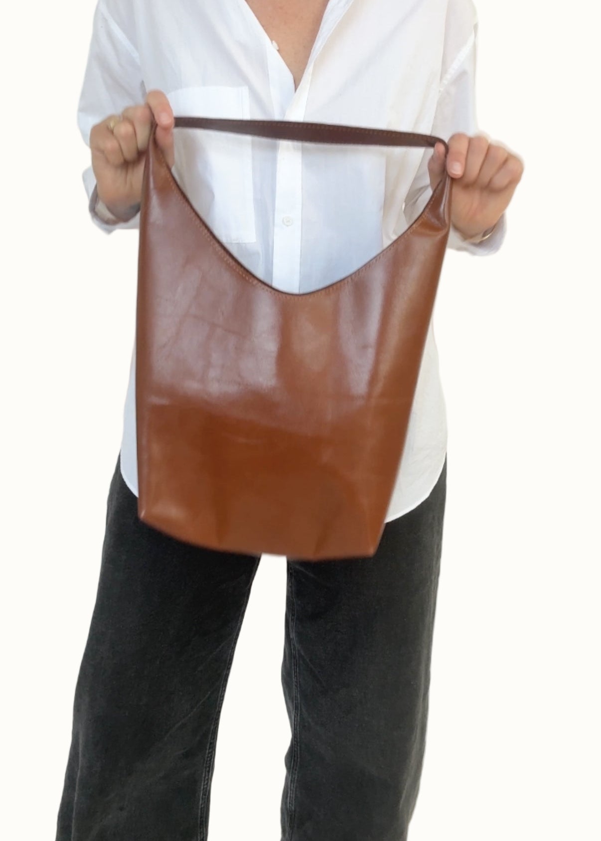 Person holding a brown leather tote bag against a white background