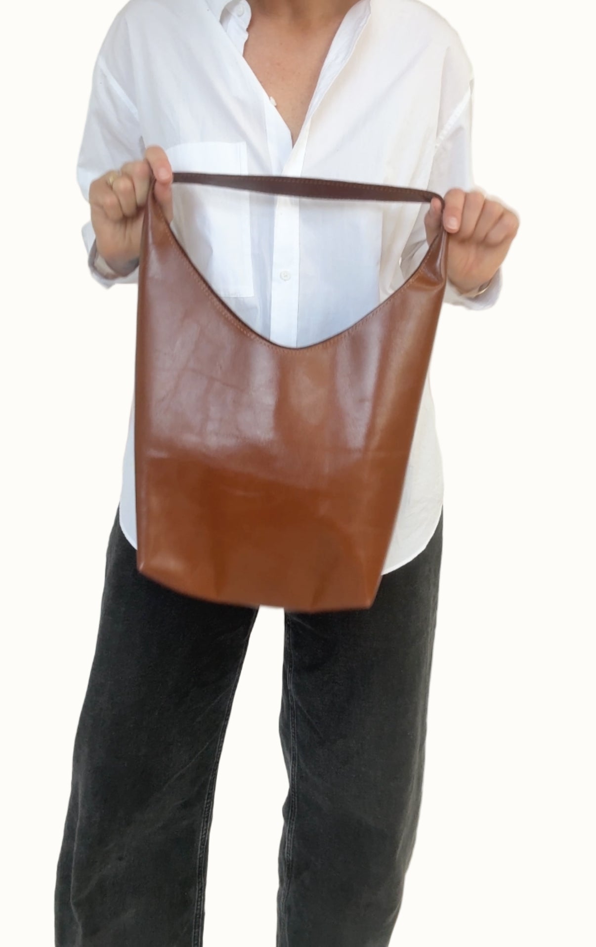 Person holding a brown leather tote bag against a white background
