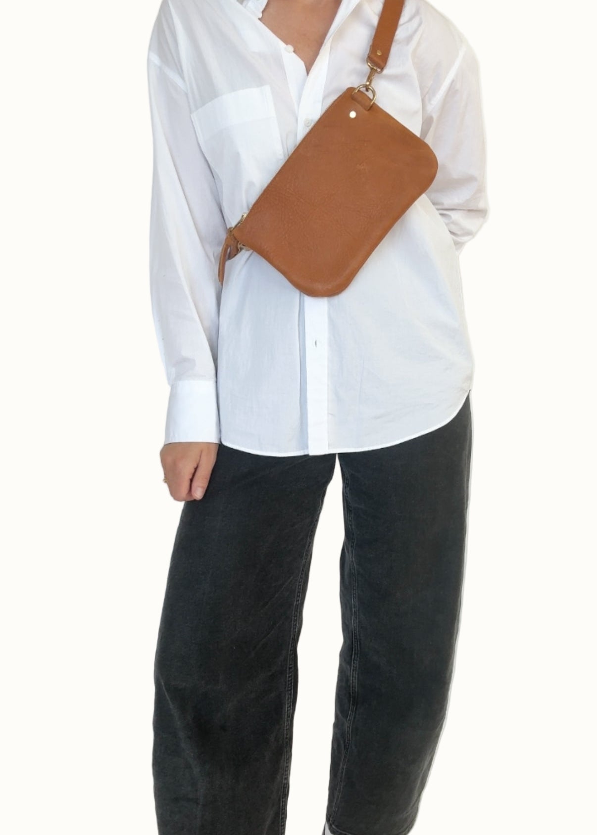 Person wearing a white shirt and black pants with a brown leather bag over one shoulder against a white background