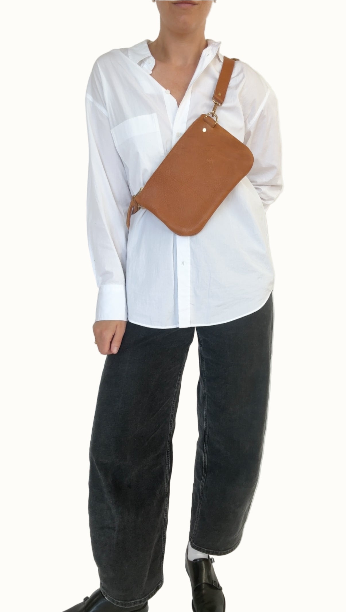 Person wearing a white shirt and black pants with a brown leather bag over one shoulder against a white background