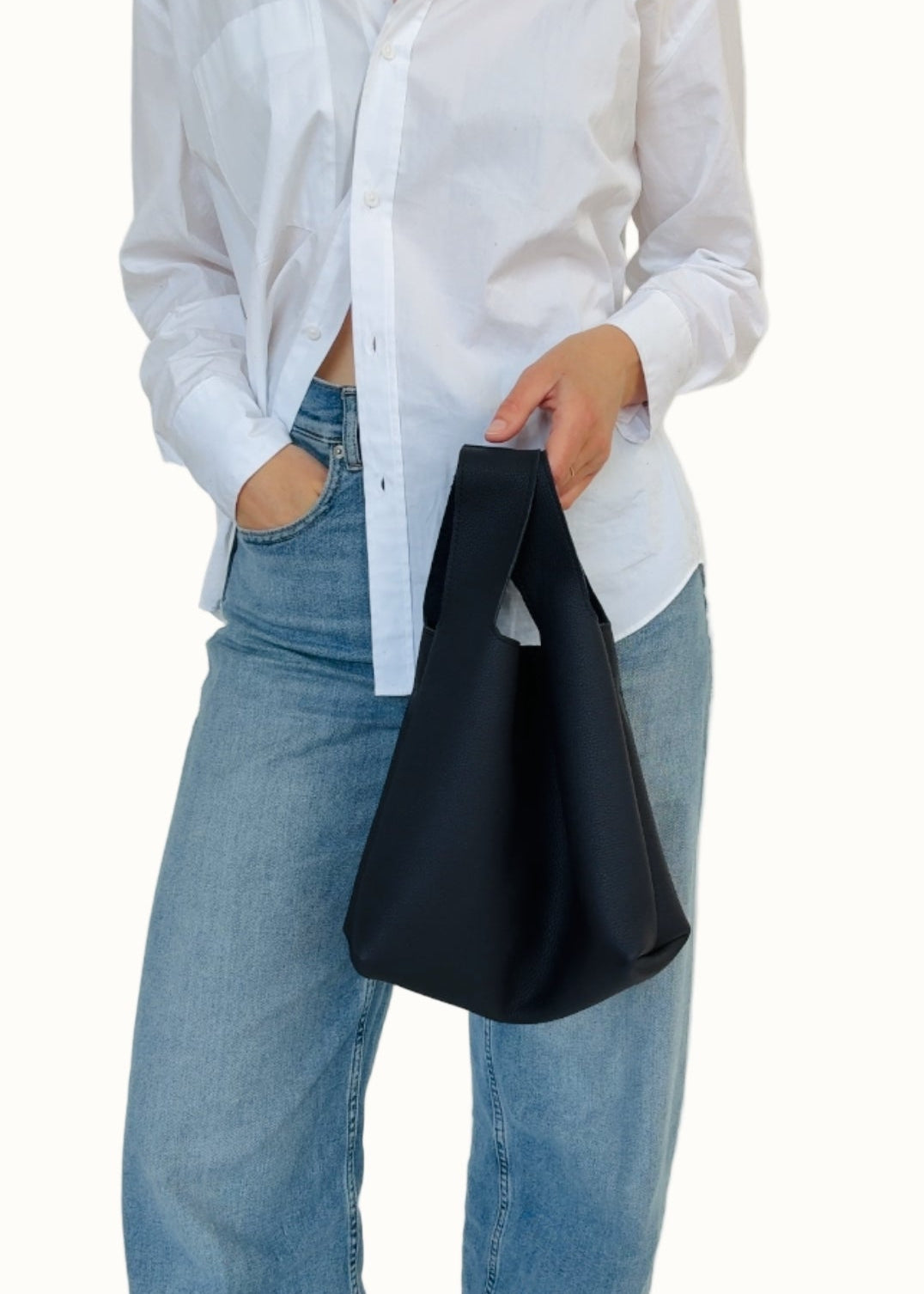Person wearing a white shirt and blue jeans holding a black bag against a white background