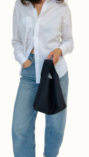 Person wearing a white shirt and blue jeans holding a black bag against a white background