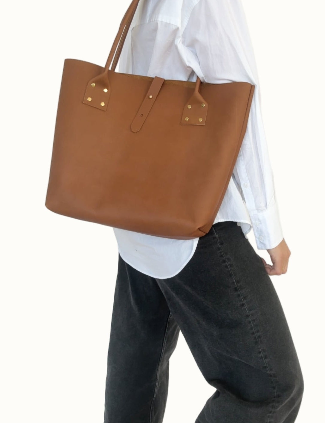 Person wearing a brown leather tote bag over one shoulder against a white background