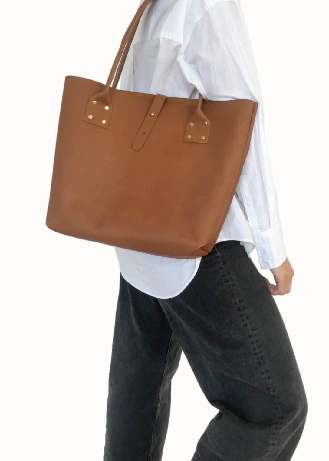 Person wearing a brown leather tote bag over one shoulder against a white background