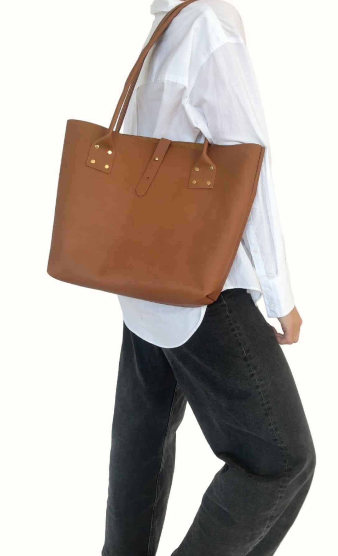 Person wearing a brown leather tote bag over one shoulder against a white background