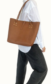 Person wearing a brown leather tote bag over one shoulder against a white background