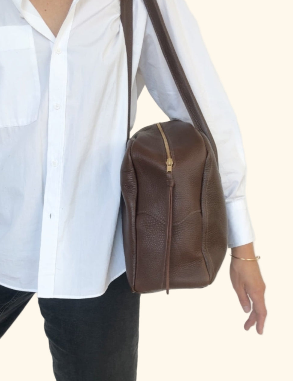 Person wearing a white shirt and black pants with a brown leather bag on a white background