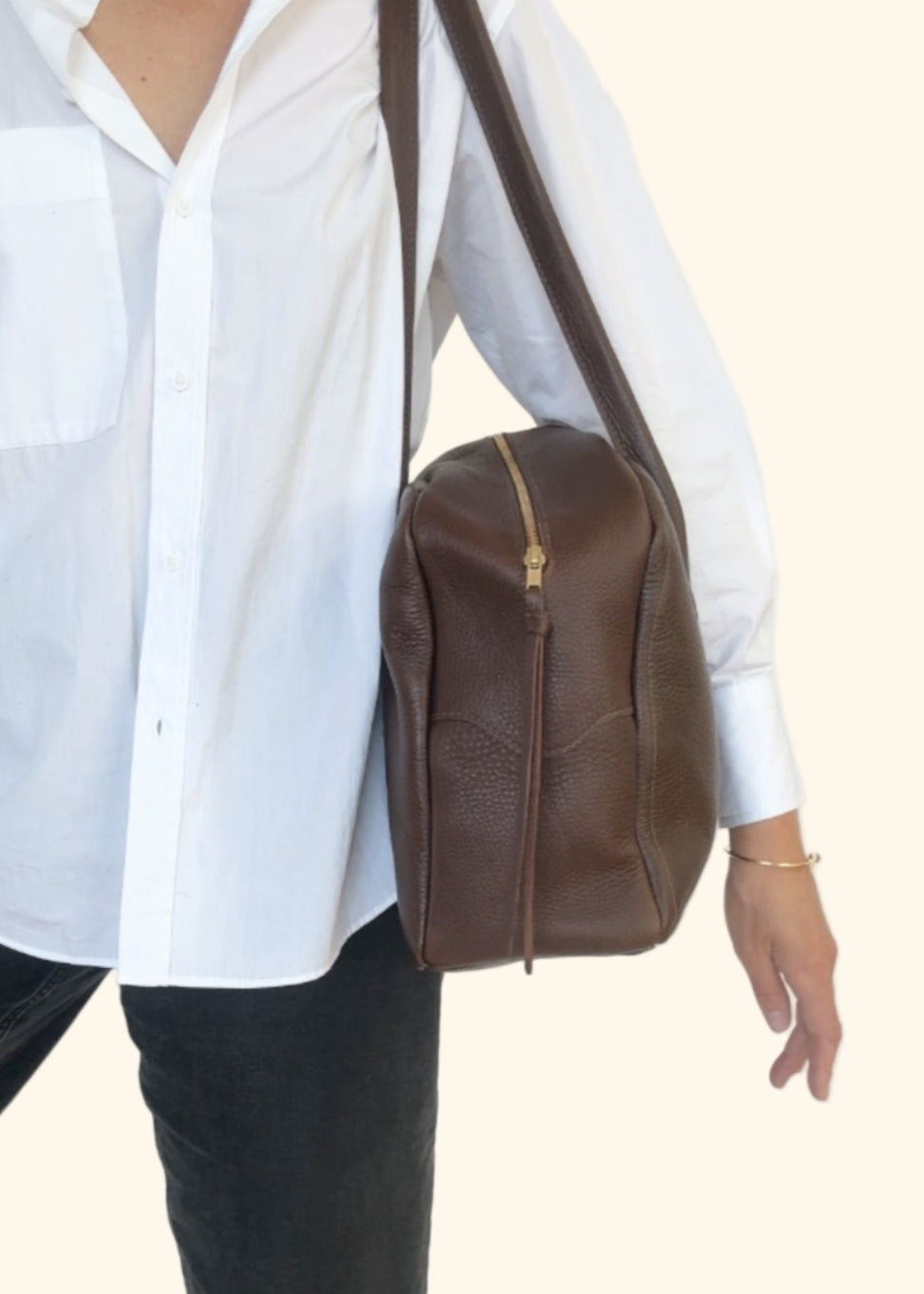 Person wearing a white shirt and black pants with a brown leather bag on a white background