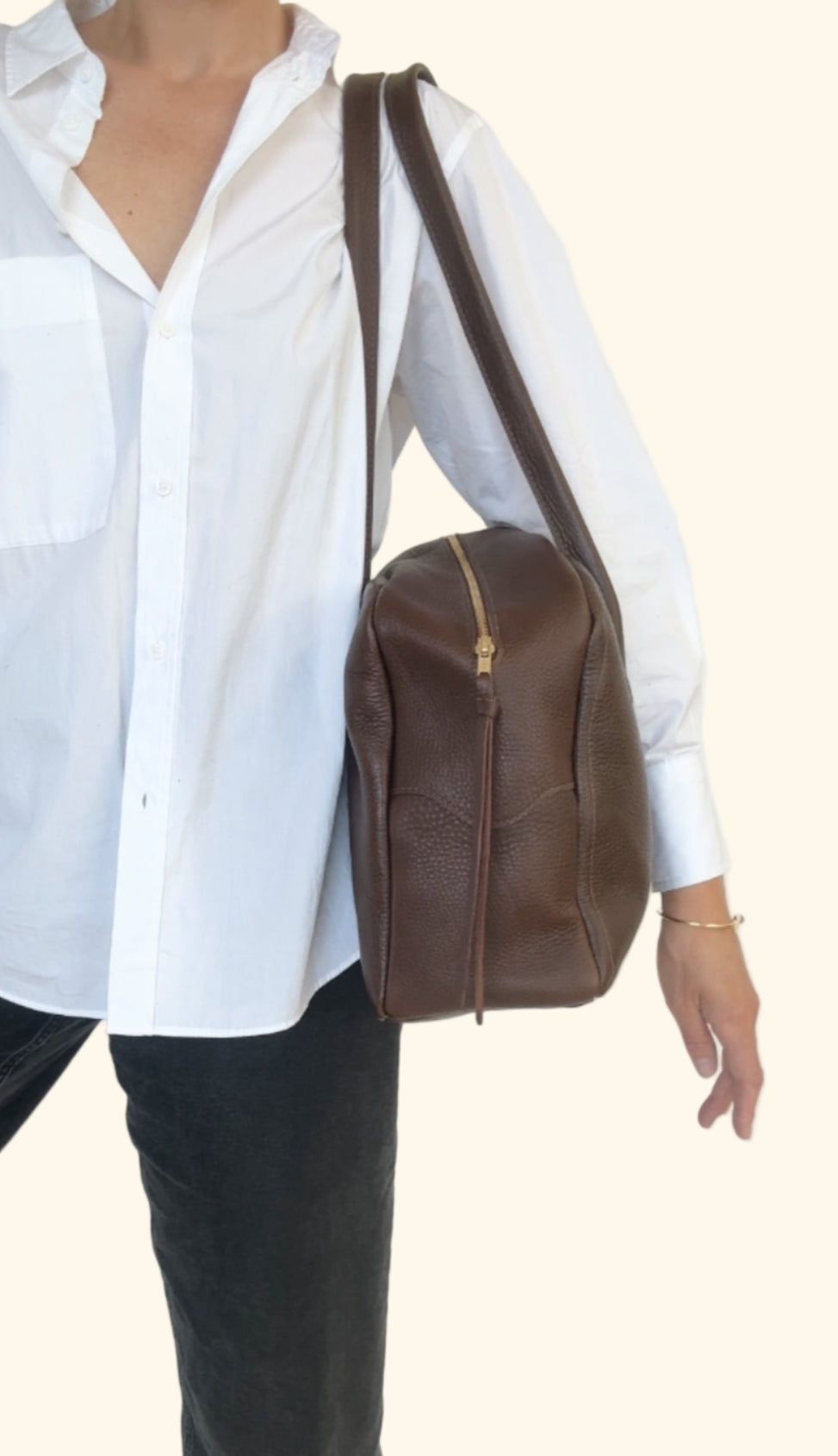 Person wearing a white shirt and black pants with a brown leather bag on a white background