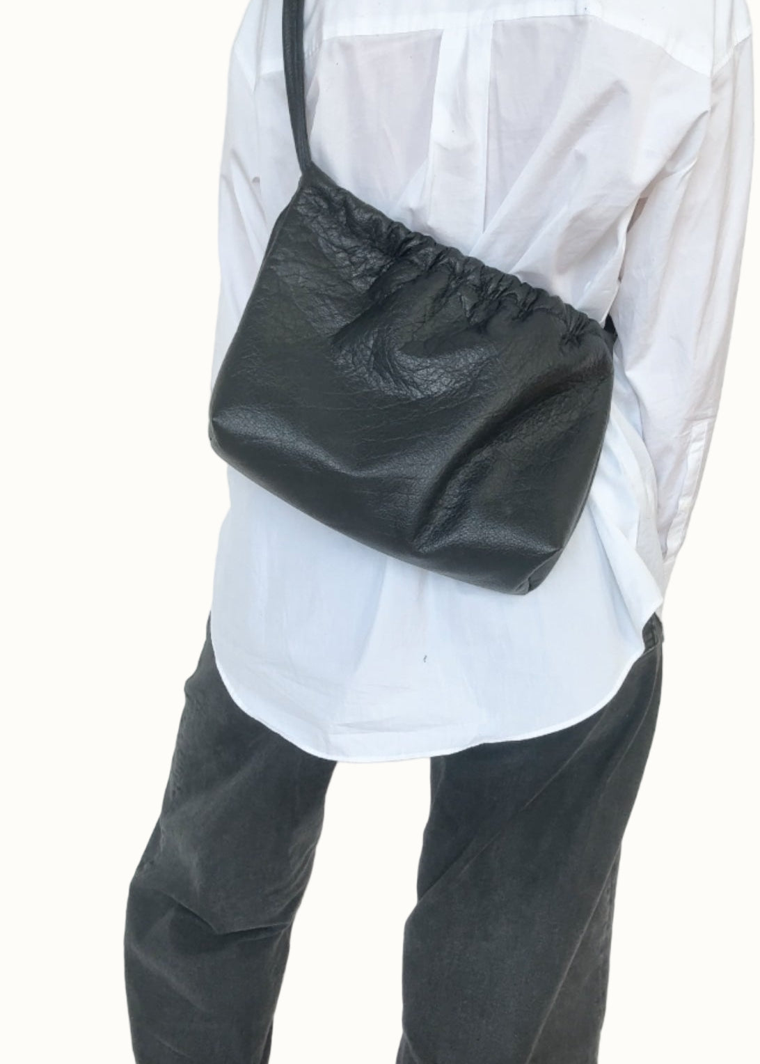 Person wearing a white shirt and dark pants with a black bag over one shoulder against a plain background