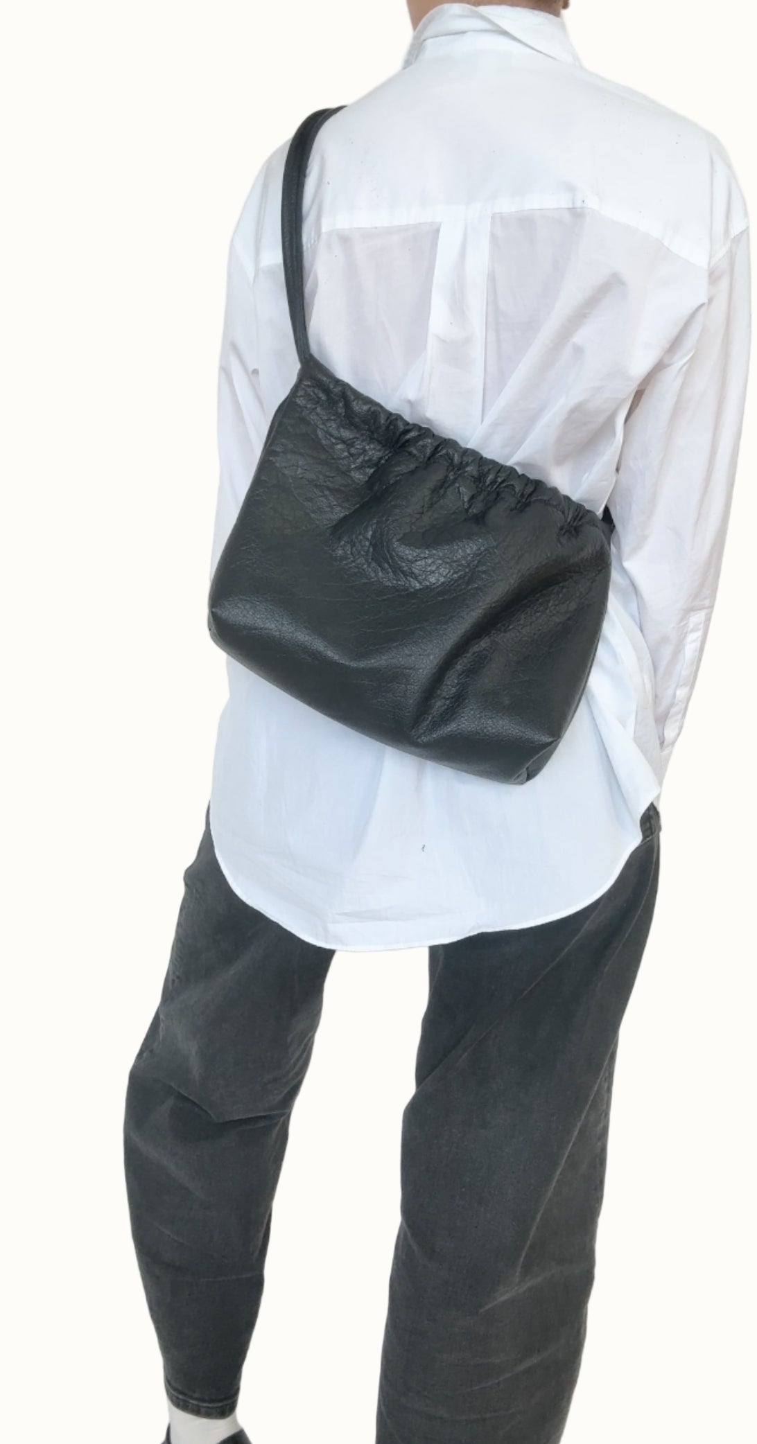 Person wearing a white shirt and dark pants with a black bag over one shoulder against a plain background