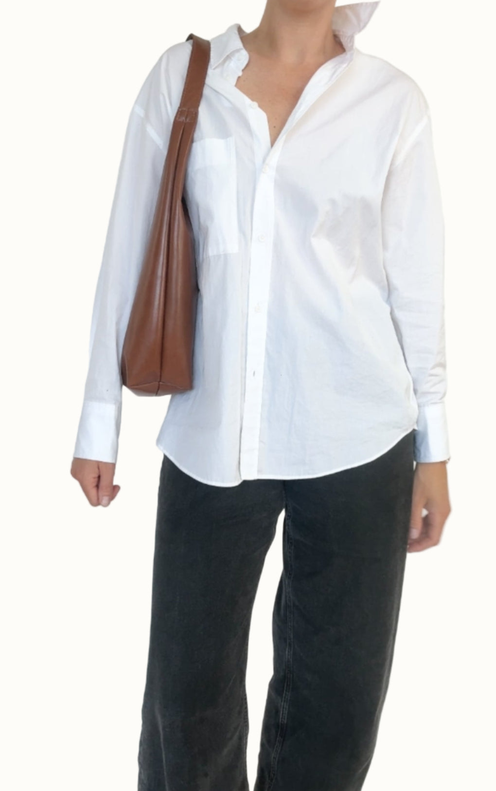 Person wearing a white shirt and black pants with a brown bag on a plain background