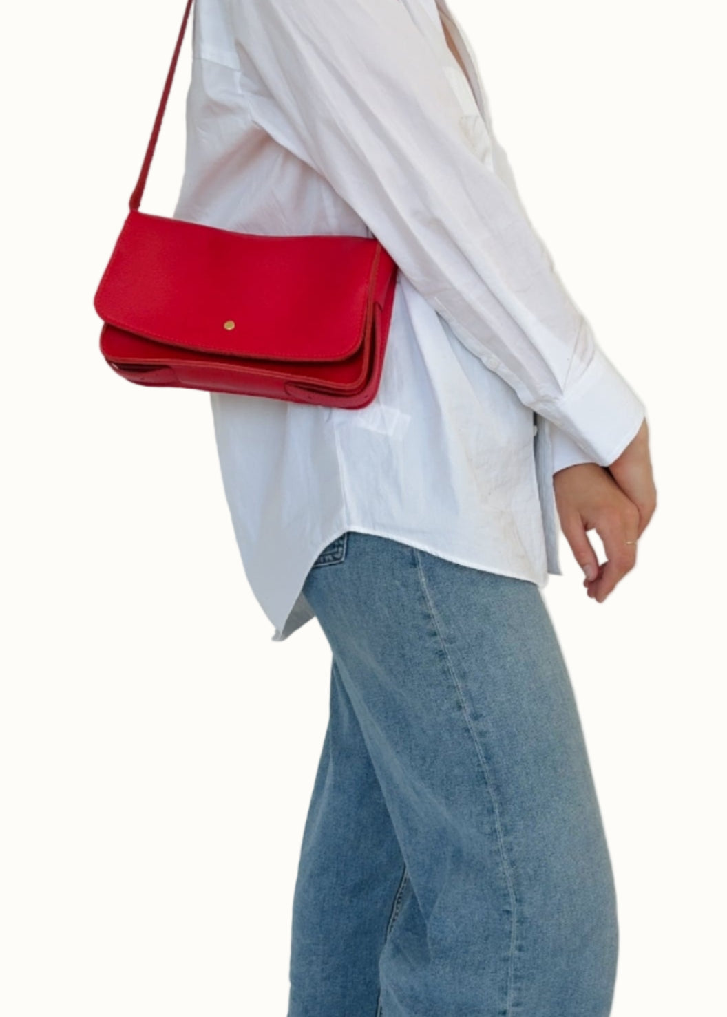 Person wearing a white shirt, blue jeans, and black shoes with a red handbag on a plain background