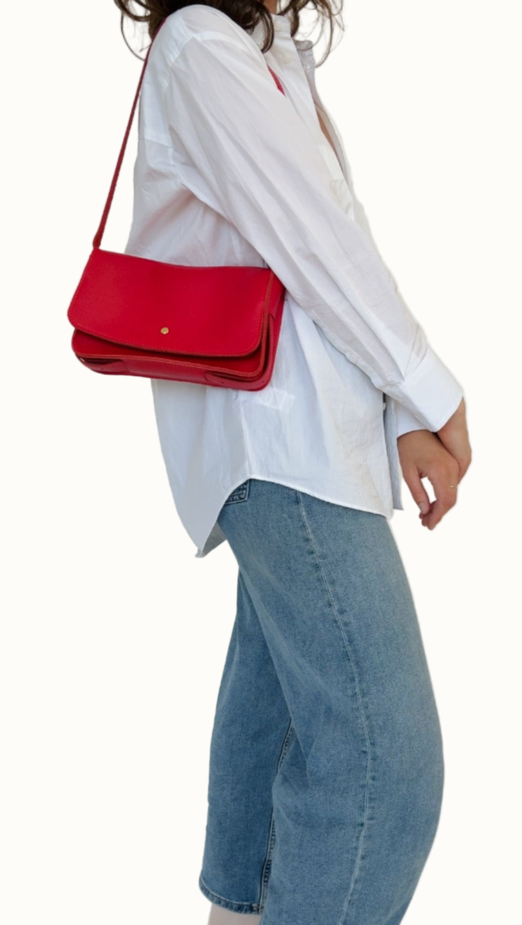 Person wearing a white shirt, blue jeans, and black shoes with a red handbag on a plain background
